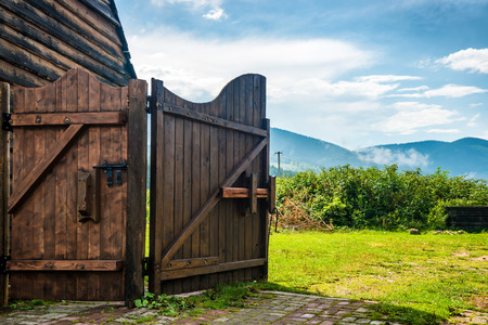 Rural wooden gate and green lawn with grass, mountains, blue skyの写真素材
