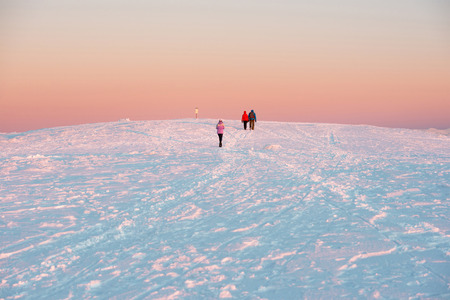 People walking at sunset in winter mountains covered with snow.