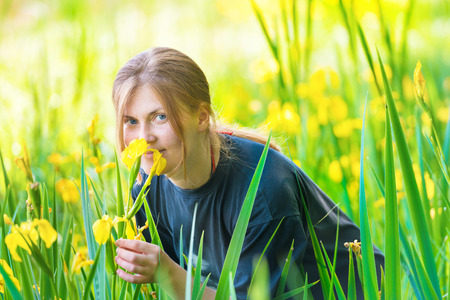 Pretty blond woman smells yellow flowers on the sunny green fieldの写真素材