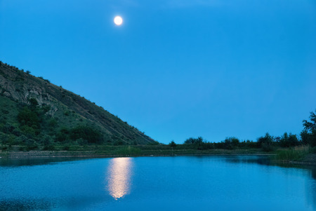 Landscape with moon above the lake. Dark blue night and moonlight reflection in waterの写真素材