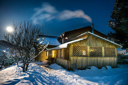 Wooden country house in snow at winter night under blue dark sky with stars and moonの写真素材