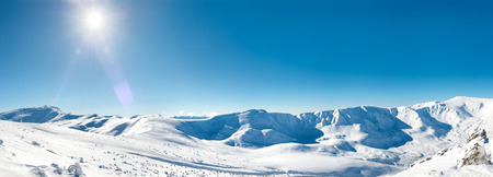 Panorama of white winter mountains with snow and bright shining sun and sunraysの写真素材