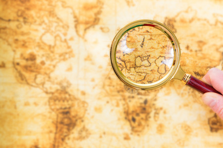 Old map and magnifying glass in a hand explored it. Vintage travel backgroundの写真素材