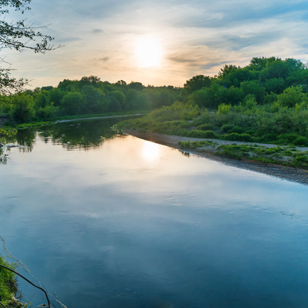 Sunset over river. Landscape with green trees, dramatic sky, clouds, sun and sunrays