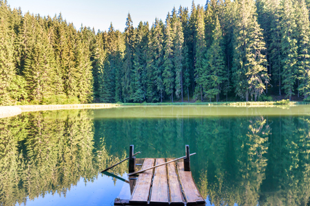 Forest lake in the mountains with blue water, wooden bridge, morning light and shining sunの写真素材