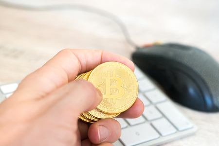 Several golden bitcoins in a hand near white keyboard and computer mouse. Electronic money mining conceptの写真素材