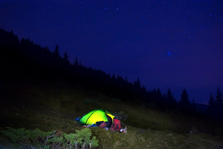 Illuminated orange camping tent under stars at nightの写真素材