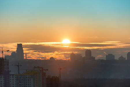 Panoramic view of sunset in the city with silhouette of buildings and industrial cranesの写真素材