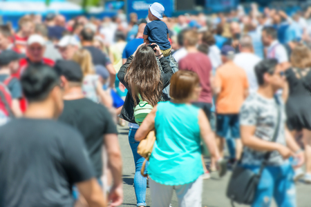 Woman with smartphone and child in crowd of people walking on city street