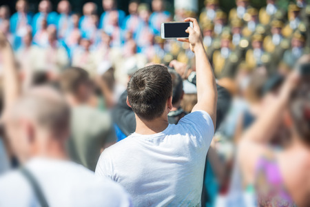 Young man with smartphone in a hand taking picture in crowd of peopleの写真素材