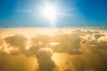 Airplane view of beautiful landscape with gold colored clouds, ocean with mountain peak and bright sunset shining sunの写真素材