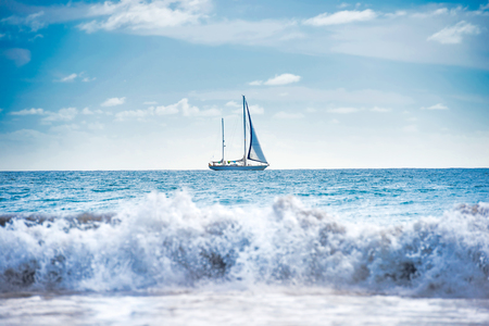 Seascape with white sailboat, blue water and surf wave on foregroundの写真素材