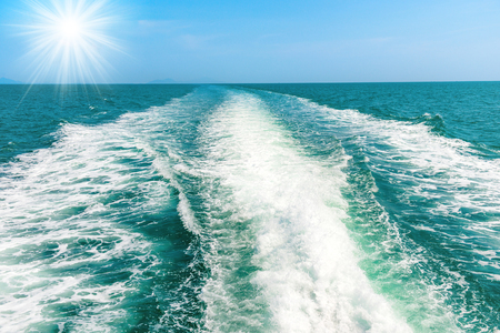 Wave from speed boat on blue sea with sun rays on skyの写真素材