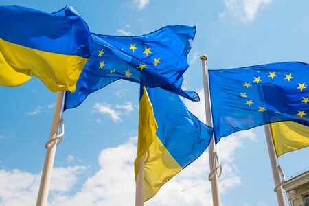 Row of flagpoles with European Union and Ukraine flags fluttering by wind on blue sky backgroundの写真素材