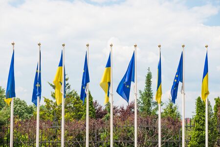 Row of flagpoles with European Union and Ukraine flags fluttering by wind on blue sky background