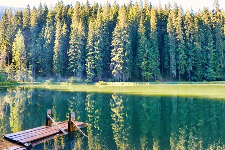 Forest lake in the mountains with blue water, wooden bridge, morning light and shining sunの写真素材