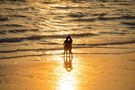 Silhouettes of people walking on beach and taking photo at beautiful sunsetの写真素材