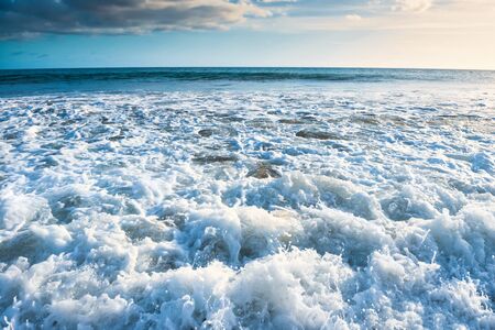 Seascape with surf waves, bright sky and white cloudsの写真素材