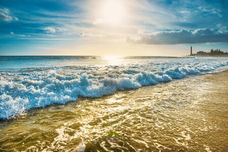 Sea, sand beach with surf waves and lighthouse on background. Maspalomas, Gran Canaria island, Spainの写真素材