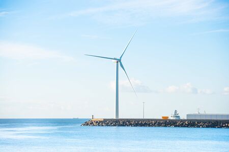 View of sea bay and large windmill at edge of stone breakwater の写真素材
