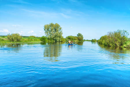 Couple at kayak trip on blue river landscape and green forest with trees blue water clouds skyの写真素材