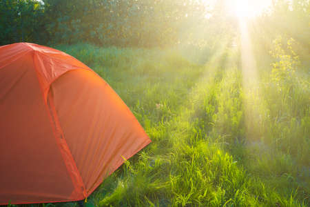 Orange tent camping at sunset in forest and green grass field and sun raysの写真素材