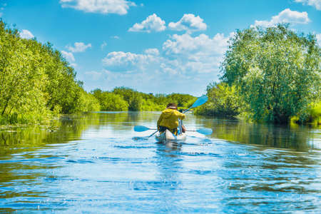 Couple at kayak trip on blue river landscape and green forest with trees blue water clouds skyの写真素材