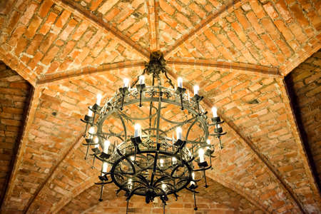 Old metal chandelier on brick ceiling in medieval castleの写真素材