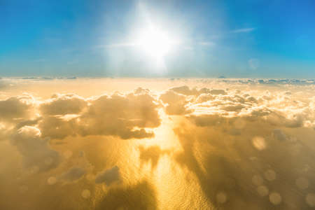Airplane view of beautiful landscape with gold colored clouds, ocean with mountain peak and bright shining sunの写真素材