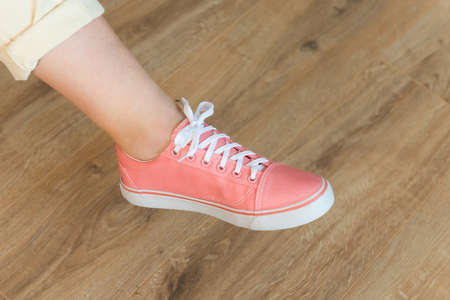 Casual pink shoes sneakers on womenâ€™s feet on wooden floor background