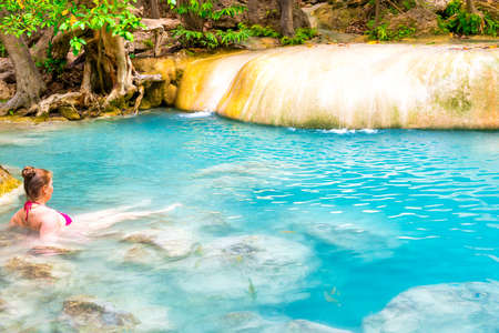 Red haired young woman in pink bikini swimsuit swims in emerald blue water of tropical lake. Erawan National park, Kanchanaburi, Thailandの写真素材