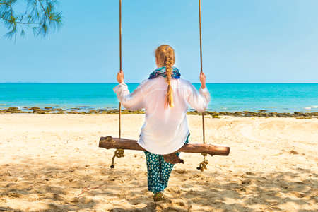Happy pretty young woman swinging on beach swing at tropical islandの写真素材