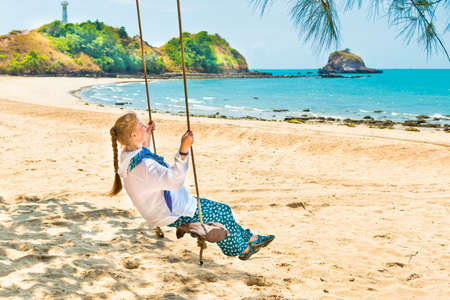 Happy pretty young woman swinging on beach swing at tropical islandの写真素材