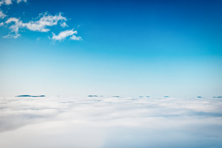 Top peaks of mountains in white clouds and blue skyの写真素材