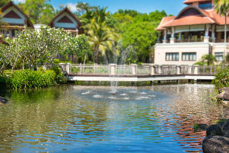View of beautiful green pond with fountain and buildings of luxury hotel at tropical resortの写真素材
