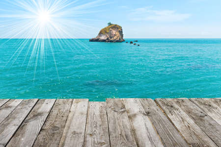 Rock island in blue sea, view from wooden tableの写真素材