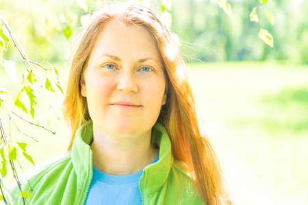Pretty young woman face with red hair and green sunny background in parkの写真素材
