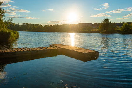 Wooden mooring bridge at water sunset with sun reflection on waterの写真素材