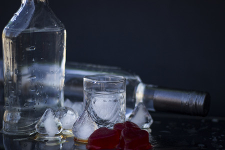 A bottle of vodka and a glass with ice, alcoholic drink, close-up on a black backgroundの写真素材