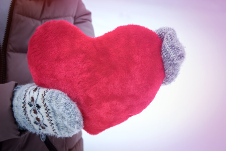 The woman in mittens holding a big red heart on a snow background. for Valentine's dayの写真素材
