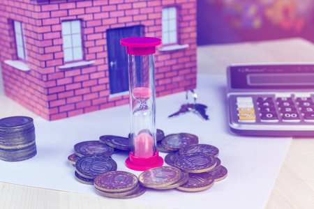 Hourglass house money and calculator on the table. The concept of timeの写真素材