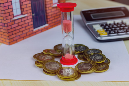Home and money, hourglass and calculator on table close-up