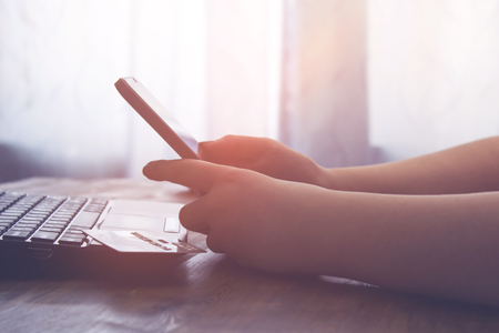 A woman holds a smartphone sitting at the table. vintage effectの写真素材