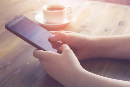 Hands holding smartphone and cup of coffee on the table. vintage effectの写真素材