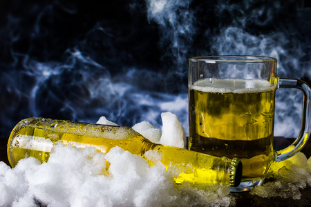 Bottle and beer mug in the snow on a background of smokeの写真素材