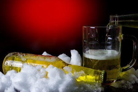 Bottle and beer mug in the snow on the red and black backgroundの写真素材
