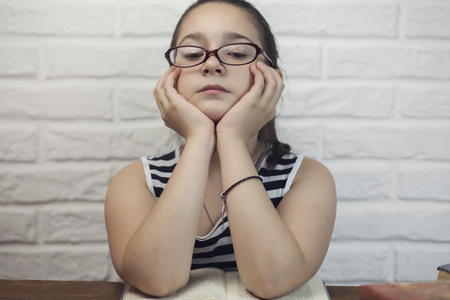 Pensive young schoolgirl sitting for desk with booksの写真素材