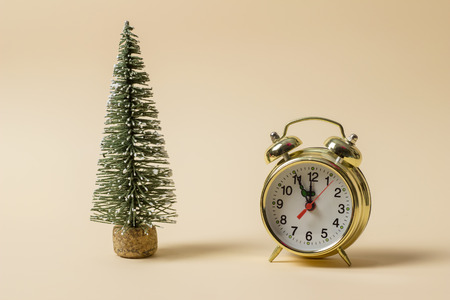 Golden watch and a miniature Christmas tree on a light brown backgroundの写真素材