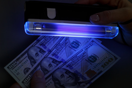 Checking a few hundred dollar bills on a banknote detector, against a dark background