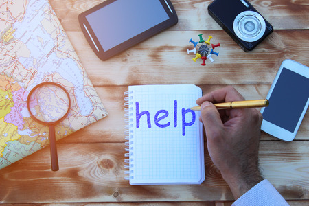 The inscription HELP in a notebook that lies on a wooden table with a phone and a map of the worldの写真素材